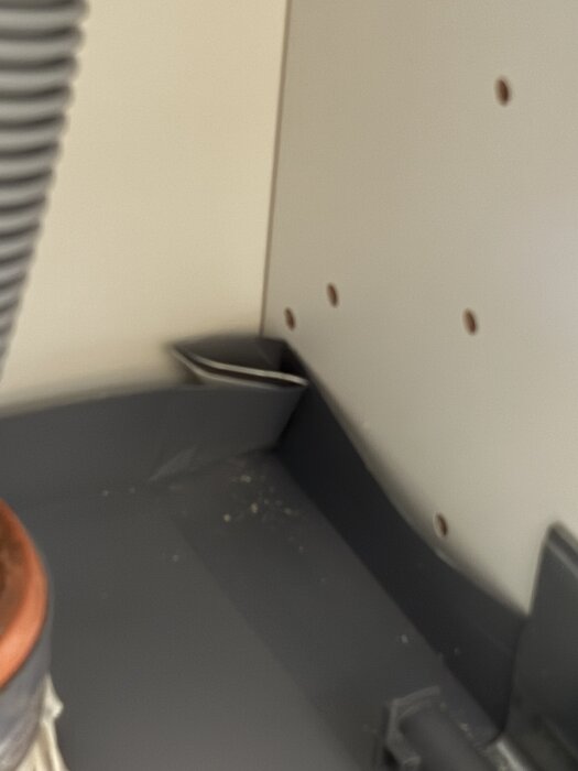Tätningar runt avlopp under diskho med slarvig plastmatta som inte når hela vägen bak, vilket kan orsaka potentiellt läckageproblem.
