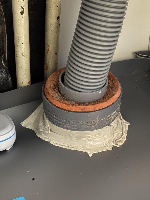 Grå slang installerad i diskbänkskåp med slarvig tätning och plastmatta som inte når hela vägen. Potentiell risk för läckage bakom installationen.