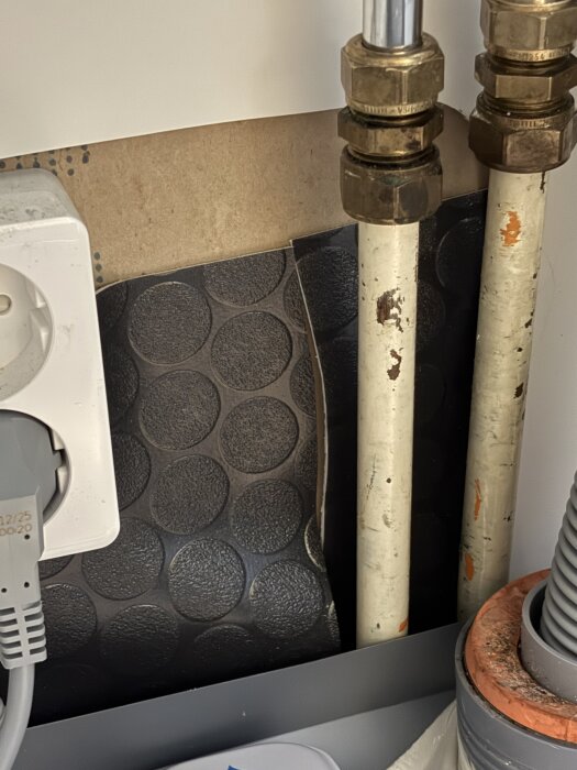 Installationsområde under diskho med slarvigt tätade rör och en plastmatta som inte når väggen, vilket visar potentiell risk för vattenläckage.