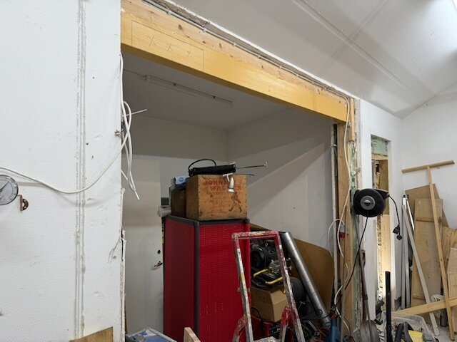 Garaget med en öppning där en limträbalk stöds av stolpar i varje ände. Verktyg och material är staplade vid sidan, balken markerad för modifiering.