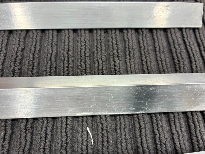Aluminiumlister från SP-fönster med vita prickar på ytan, liggande på en mörk ribbad bakgrund.