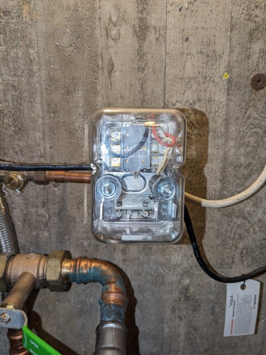 Tryckströmbrytare installerad på en vägg, ansluten till kablar och rörledningar.