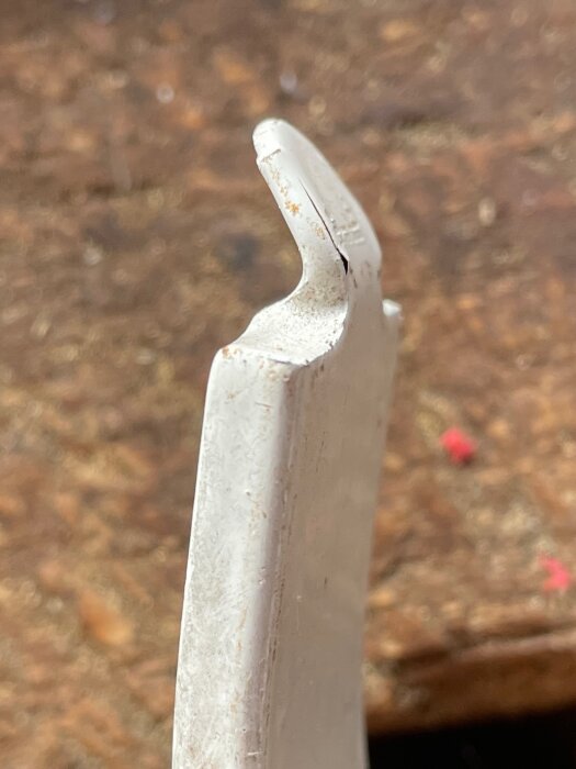 Närbild på en vit, sliten del av en metallkrok med en böjd ände mot en suddig träbakgrund.
