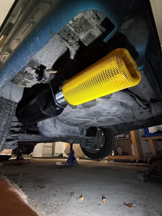 Underrede av bil med nytt avgassystem monterat, gul skyddshylsa på dämpare, bil på pallbockar i garage.