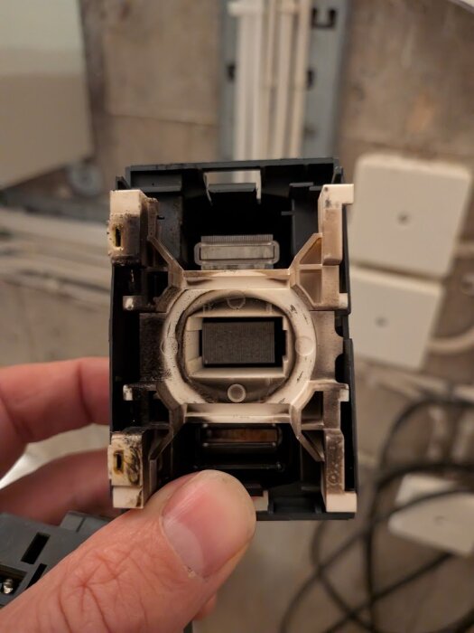 Närbild på en hand som håller en kontaktor med sotmärken och tecken på slitage. Kontaktorn verkar vara från ett pumprelaterat system.