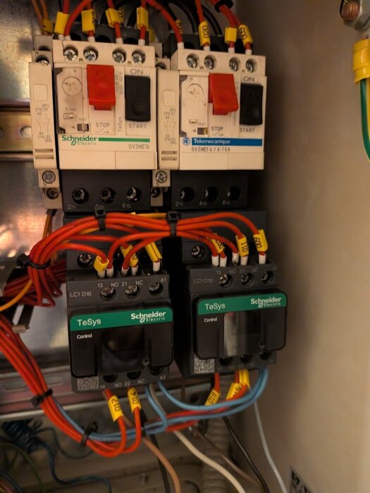 Två Schneider Electric startapparater och kontaktorer med färgkodade kablar för anslutning, märkta med TeSys och GV2ME, i ett elskåp.