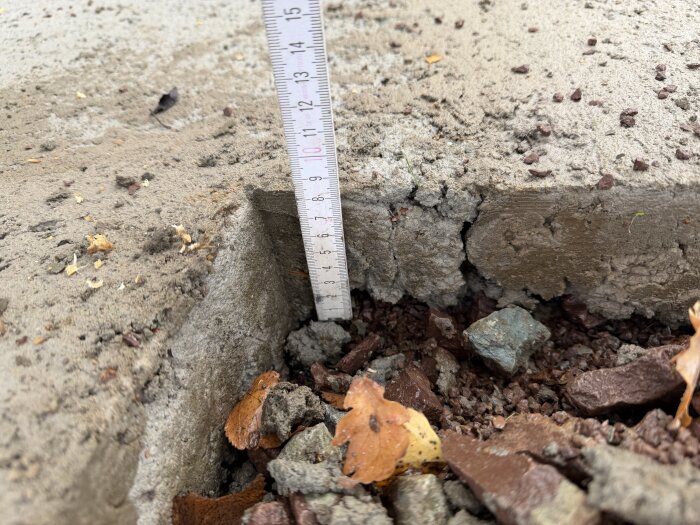Betongsula med en linjal visar djupet. Sidan av sulan och olikstor kross syns nedanför på byggarbetsplats.