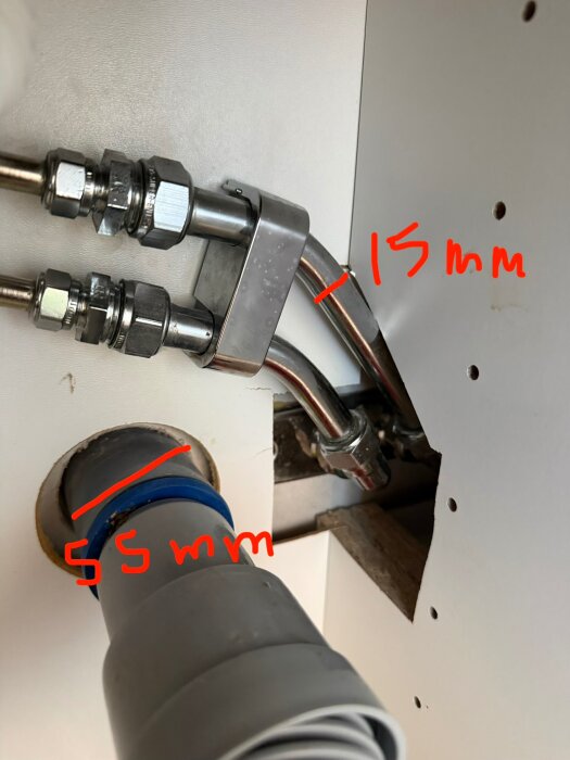 Vattenrör och anslutningar i ett skåp med handskrivna måttangivelser, 15 mm och 55 mm, markerade på bilden.
