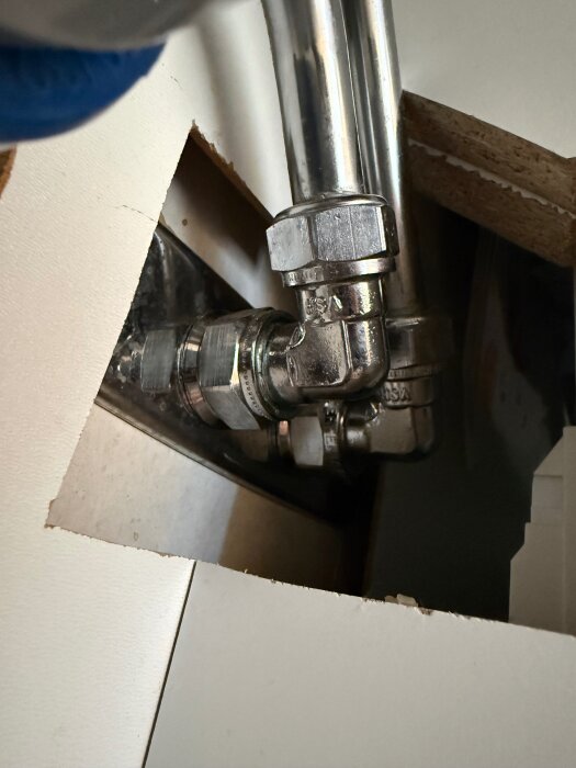 VVS-rör med kopplingar synliga genom ett hål i ett skåp, visar installation eller reparation av rörsystem.