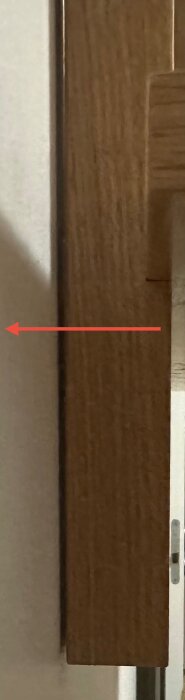 Träbit på vägg där plugg har flyttat sig några millimeter utåt. En röd pil pekar mot mellanrummet som har skapats mellan träet och väggen.