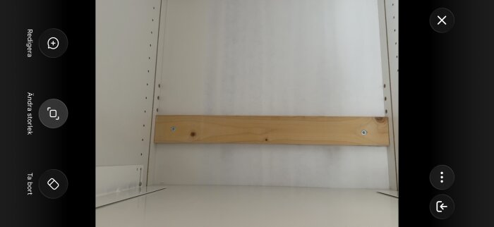 Inre av ett skåp med en träregel fastskruvad horisontellt på den vita bakväggen.