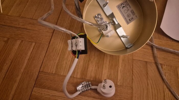 Ny lampa med metallarmatur och anslutna kablar. En jordad stickpropp ligger på golvet bredvid lampan.