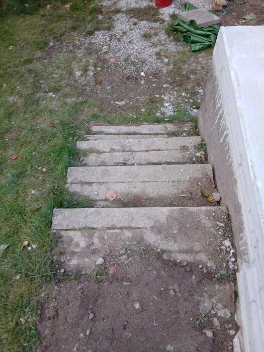 Betongtrappa under konstruktion, omgiven av jord och gräs. En mur syns till höger, och byggmaterial ligger ovanpå.