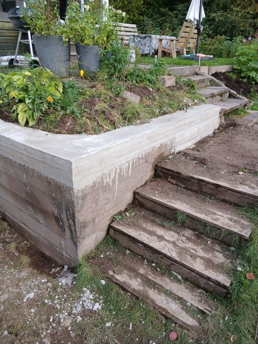 Betongtrappa under konstruktion vid en mur med omgivande växtlighet, sittmöbler och trappa i bakgrunden; diskuteras byggmetoder.