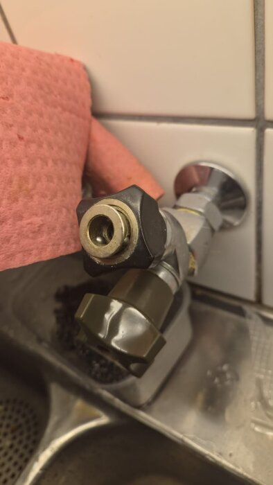 Vattenkran med ventil och slanganslutning ovanför en diskbänk, delvis täckt med rosa trasa.