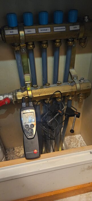 Installation av golvvärme med flera ventiler märkta för olika rum. Digital termometer visar temperaturen i systemet.