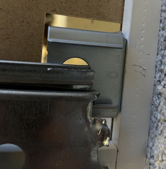 Närbild på en för kort Metod upphängningsskena bakom ett Ikea köksskåp, exponerar krokarna och visar hur skenan inte helt täcker upphängningskrokarna.