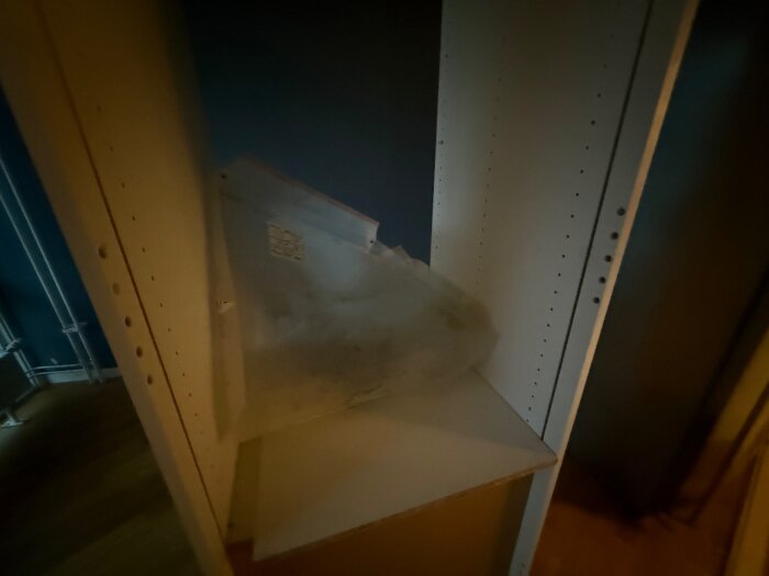 Vitt skåp med flera plugghål på insidan av sidorna; det finns en plastdetalj liggande på en hylla.