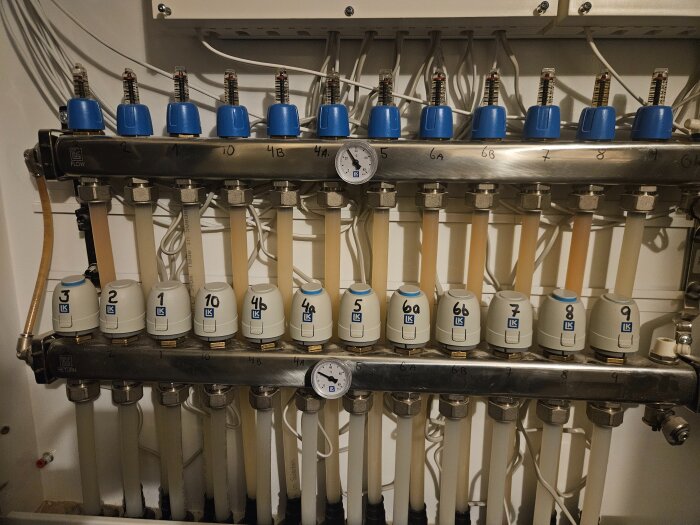 Värmefördelare med flera ventiler numrerade 1-10 och blåa termostatkåpor, där 4a är märkt som kall. Temperatur visat på mätare.