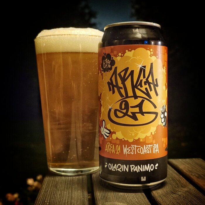 En burk med Area 24 West Coast IPA och ett fyllt glas med skum, stående på ett bord utomhus under kvällstid.