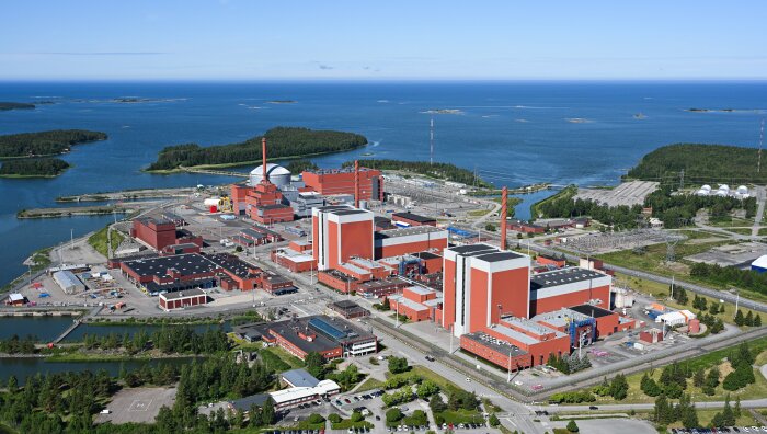 Luftfoto av Finlands moderna kärnkraftverk vid kusten, omgiven av vatten och skog.