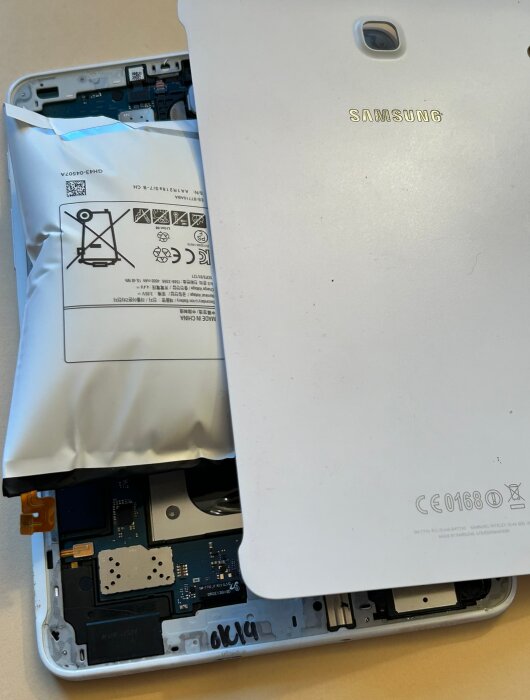 En svullen och skadad batteri på en öppen Samsung-enhet. Baksidan är delvis borttagen för att avslöja det inre.