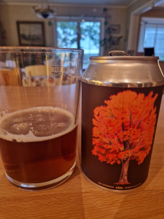Ölglas med brunlila ale bredvid en ölburk med rödbrun trädillustration från O/O Brewing Amber Ale 5.5%.