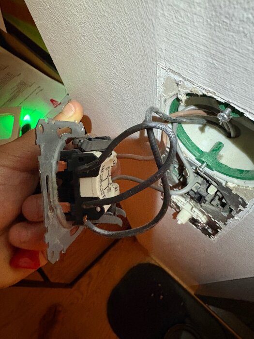 En person håller en elkoppling med flera kablar utanför en väggmonterad dosa, redo för installation av Plejd dim-02.