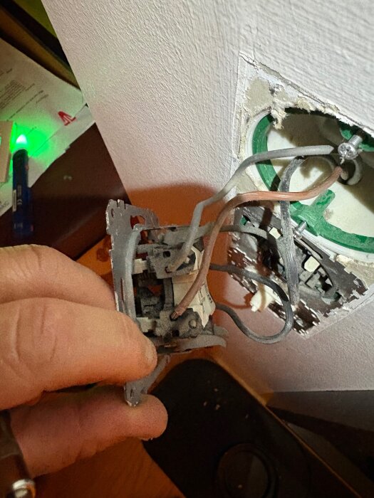 Elektrisk kopplingsdosa med exponerade kablar, hand håller i framsidan av uttaget.