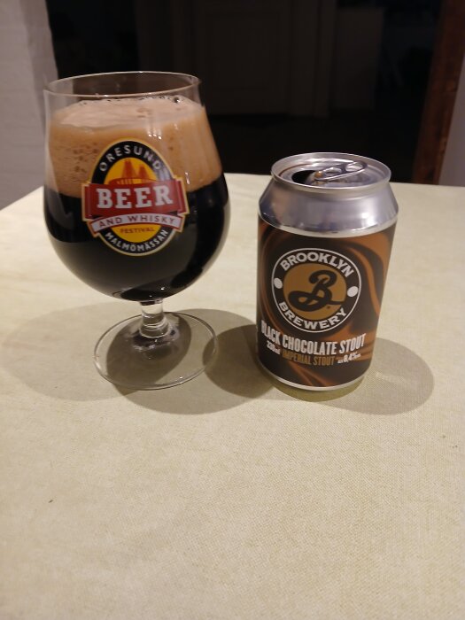 Ett glas stout med skum bredvid en burk Brooklyn Brewery Black Chocolate Stout på ett bord.
