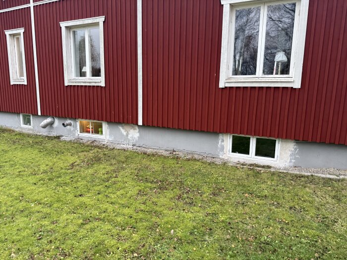 Röd träfasad med fönster och putsade fläckar på grå grund; tidigare hål för ventilation och bulkmatning.