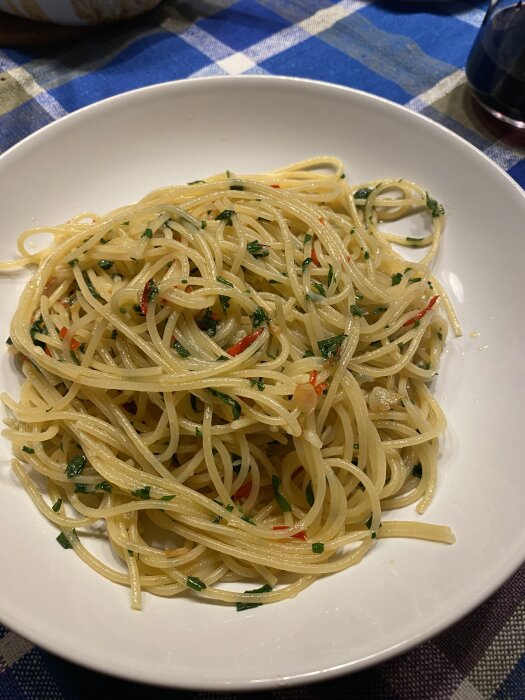 Spaghetti aglio olio con pepperoncini med olivolja, vitlök, chili, parmesan och persilja på en vit tallrik.