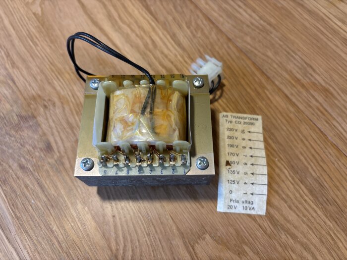Transformator av märket AB TRANSFORM typ CD 29399, monterad på trägolv, med etikett som visar olika spänningar och uttag på 20V 10VA.