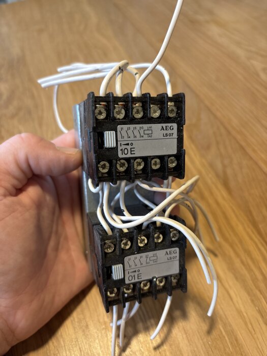 AEG kontaktorer med kablar, modell LS 07, hålls av en hand mot en träbakgrund.