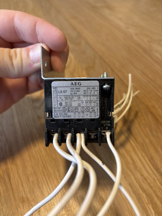 AEG kontaktor med kablar visas i närbild, hålls av en hand mot en trätopp.