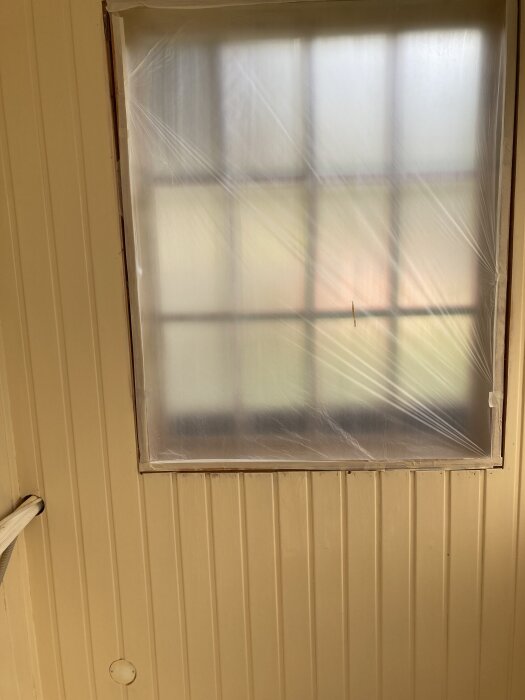 Fönster täckt med plast, omgivande väggar målade i järnoxidgul linoljefärg. Golvet är linoljepolerat i ett litet rum.
