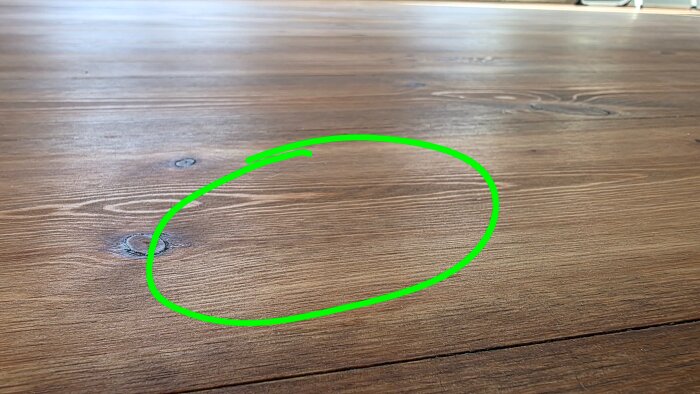 Golvyta av massiv furu behandlad med olja, markerad med en grön cirkel som visar pigmenterings- och sliprepor.
