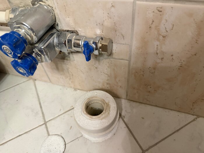 Vattenventil och golvbrunn på badrumsvägg och golv för anslutning av tvättmaskinens vattenslang och avloppsutlopp.