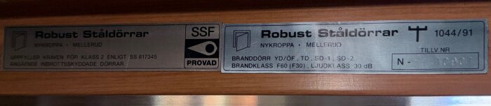 Skyltar på stål- eller säkerhetsdörr med text om robusthet, märkning av säkerhetsklass, brandklass och ljudklass från Robust Ståldörrar.