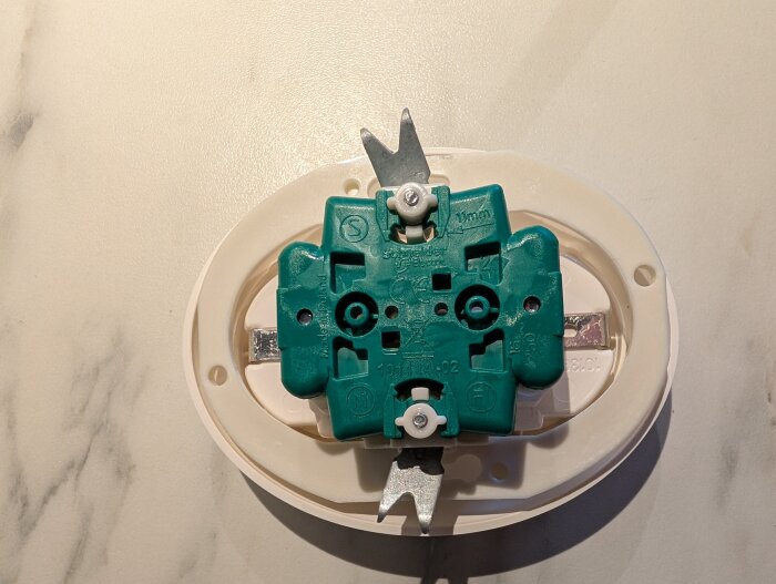 Elektrisk väggmontering med en grön insats och en vit ram, sedd ovanifrån på en marmorerad yta.