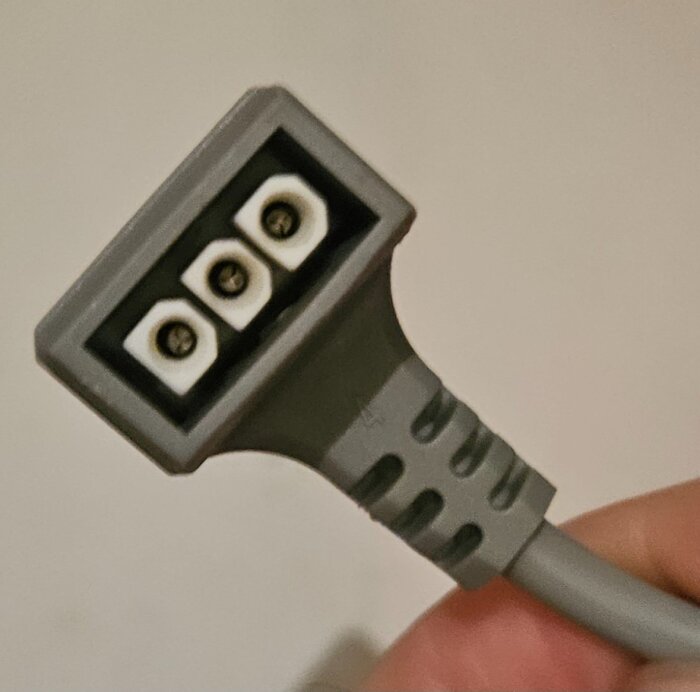 Grå strömkontakt med tre runda hål i närbild mot en ljus bakgrund.