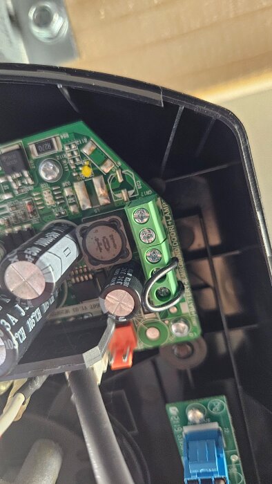 Green circuit board with connection terminals and wires inside an electronic device, showing details of electrical components and connections.