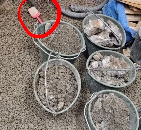 Hinkar fyllda med grus och stenar, omgivna av små grusstenar på marken, spade synlig i bakgrunden.