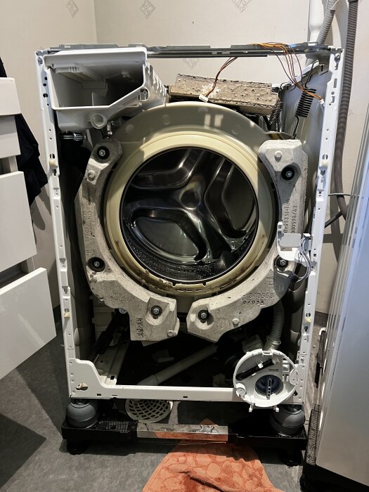Öppen tvättmaskin med borttaget hölje visar trumma och interna delar, redo för reparation eller inspektion.