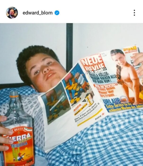 Jag vet inte vem personen på bilden är, men personen ligger med en tidning och en flaska tequila i sängen, täckt med ett blåmönstrat täcke.