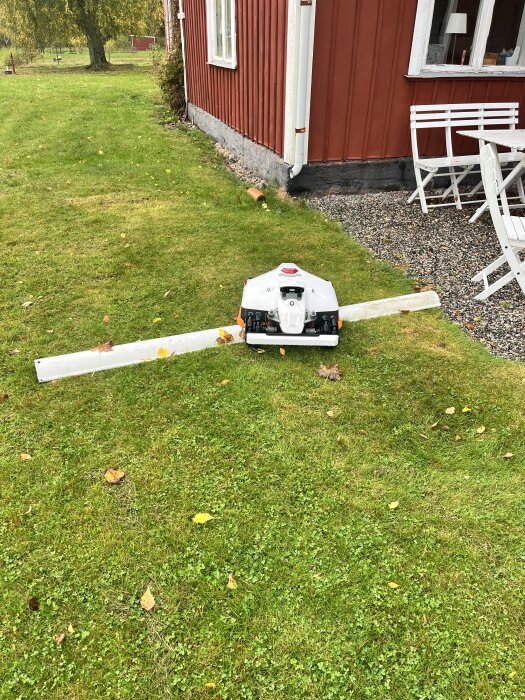 Robotgräsklippare nästintill välter hängrännan som är kopplad till stupröret vid rött hus på landsbygden.