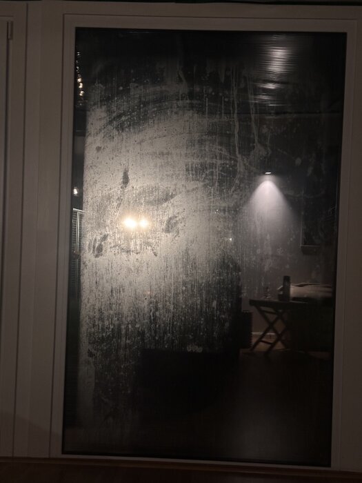 Fuktigt livmoderglas med kondens och fläckar på utsidan, inomhusbelysning syns genom glaset.