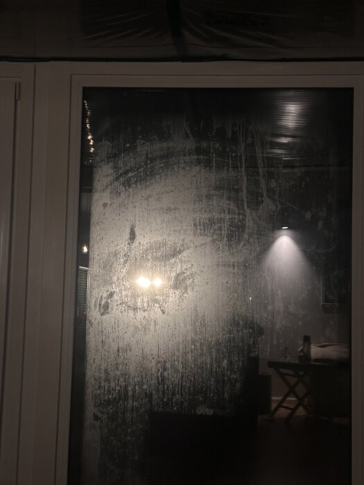 Immat fönsterglas sett utifrån med lampor speglas svagt på ytan.