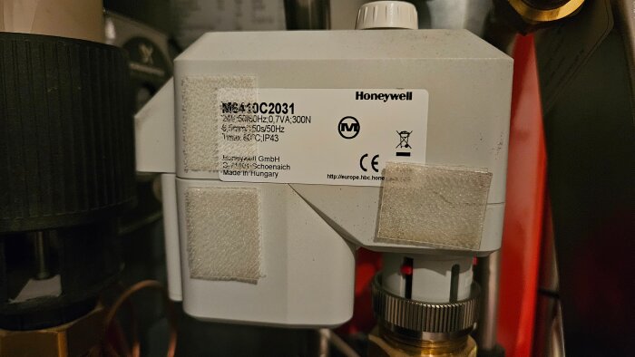 Närbild av en Honeywell ventil med etikett som visar tekniska specifikationer, placerad i ett rörsystem.