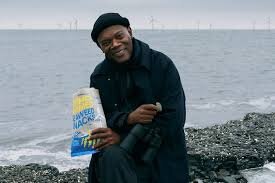 En person sitter vid havet med en påse sjögrässnacks i handen, i bakgrunden syns vindkraftverk.
